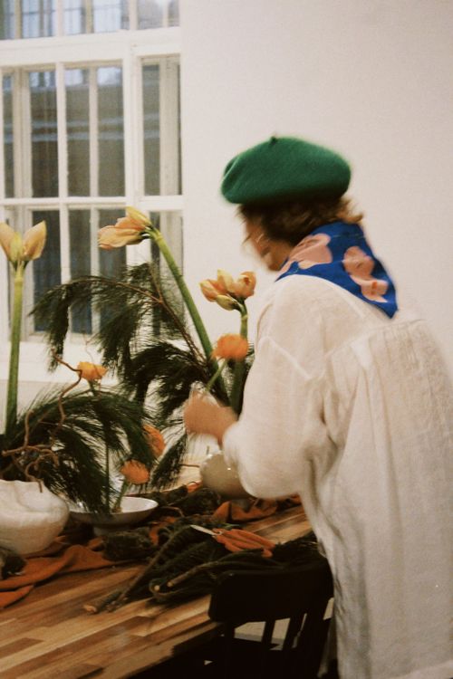 Free A woman creates a floral arrangement wearing a green beret by a window. Stock Photo