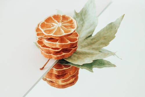 Dried Orange Fruit and Green Leaves on White Surface