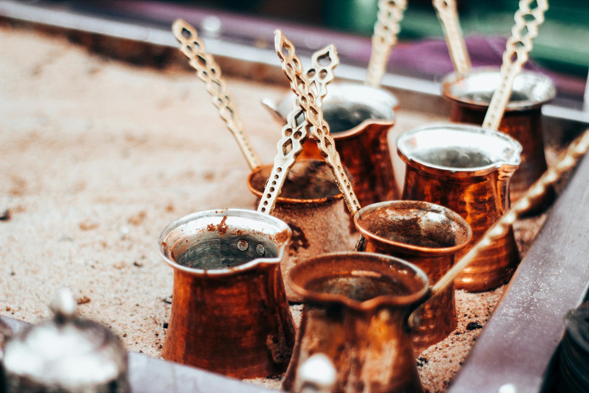 Close-up of traditional copper Turkish coffee pots placed on sand for brewing.