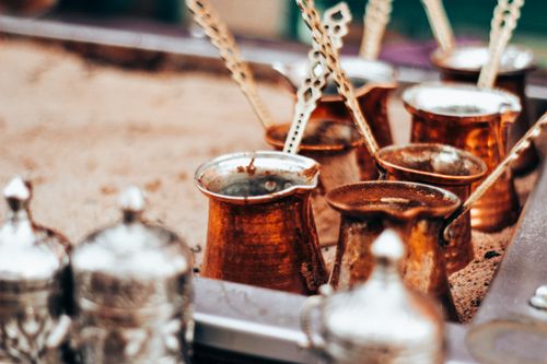 Free Close-up of traditional copper Turkish coffee pots on sand, showcasing a rustic and historical feel. Stock Photo