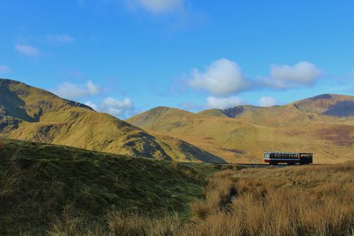 Free A picturesque train traverses the scenic Snowdonia mountains under a clear blue sky in Gwynedd, Wales. Stock Photo