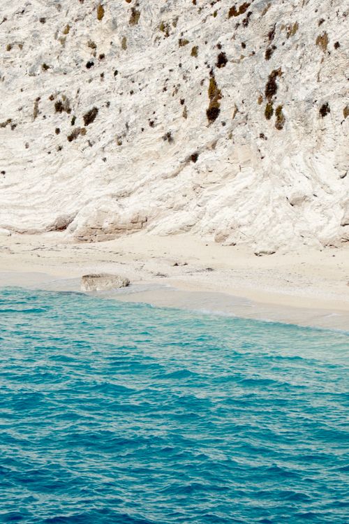 Free Pristine Greek beach with turquoise sea and rugged cliffs in the sunlight. Stock Photo