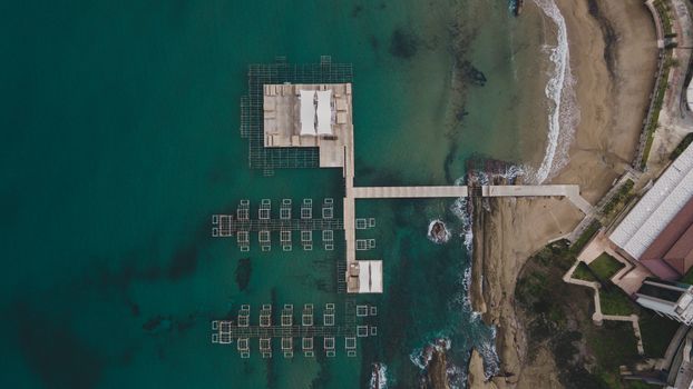 A stunning aerial view of a wooden dock extending over a serene ocean coastline.