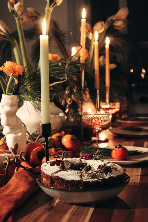 Free Warm festive holiday dinner setup with candles, cake, and fresh fruit on a wooden table. Stock Photo