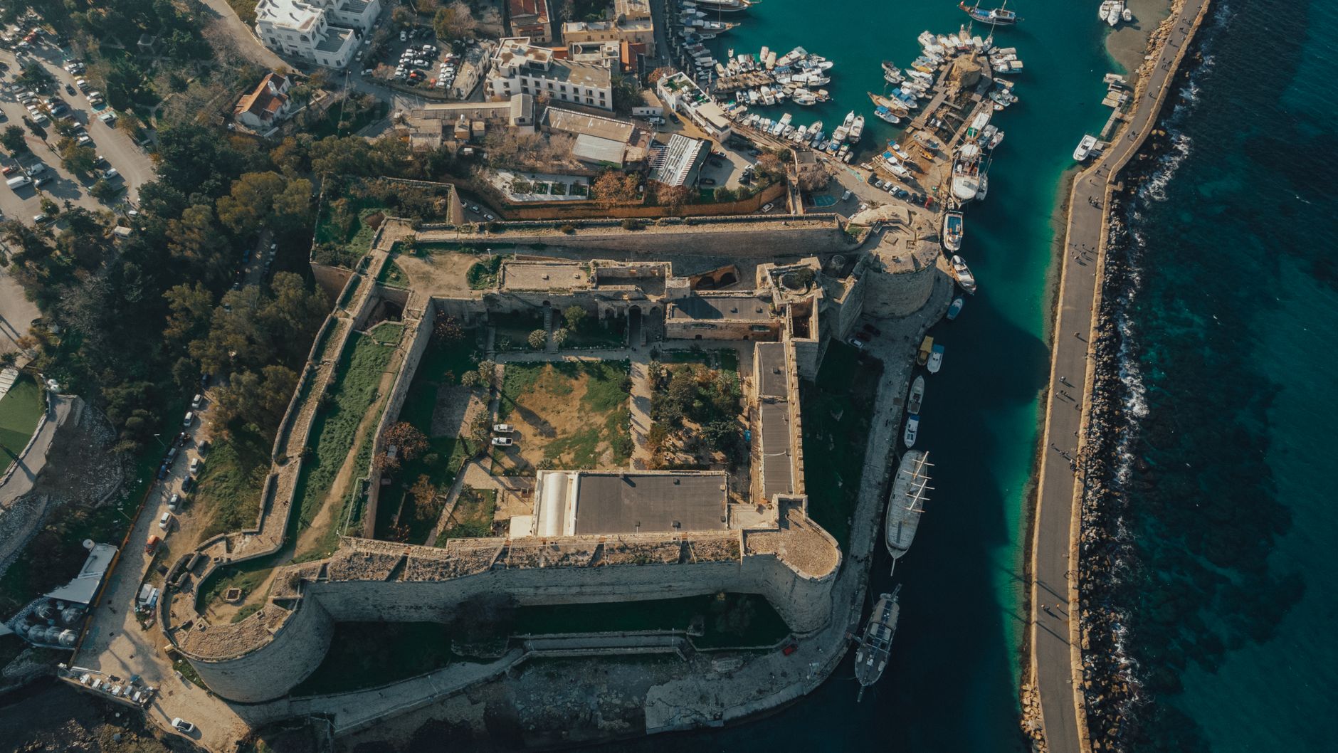 Stunning aerial view of an ancient fortress by the seaside harbor with boats and clear blue waters. — photo by Tolga Aslantürk / Pexels