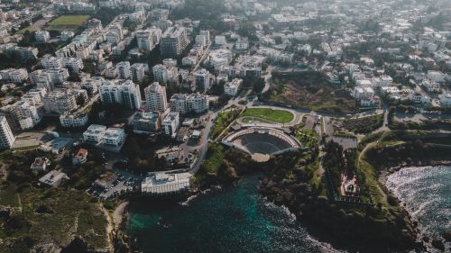 Free Stunning aerial drone shot of a coastal cityscape featuring buildings and an amphitheater by the sea. Stock Photo