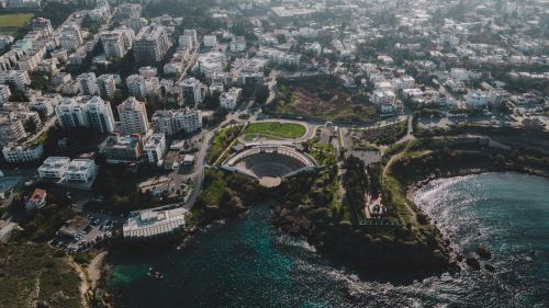 Free A stunning aerial view of a coastal cityscape featuring a prominent amphitheater and sprawling urban area. Stock Photo