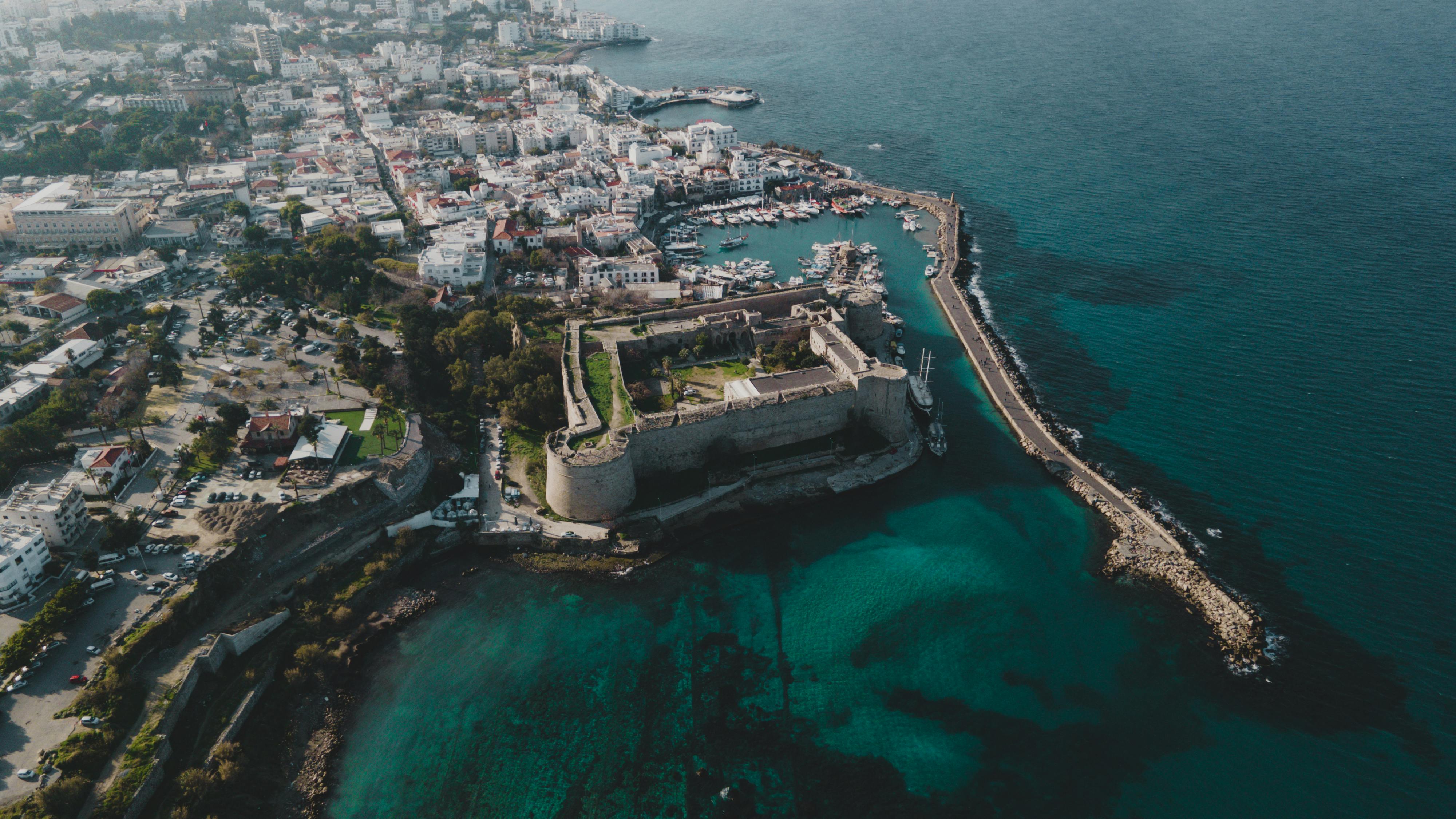 Stunning aerial view of a coastal city featuring a historic castle and clear blue waters. - Photo by Tolga Aslantürk on Pexels