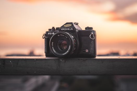 Close-up of a Yashica camera on railing against a colorful sunset background.