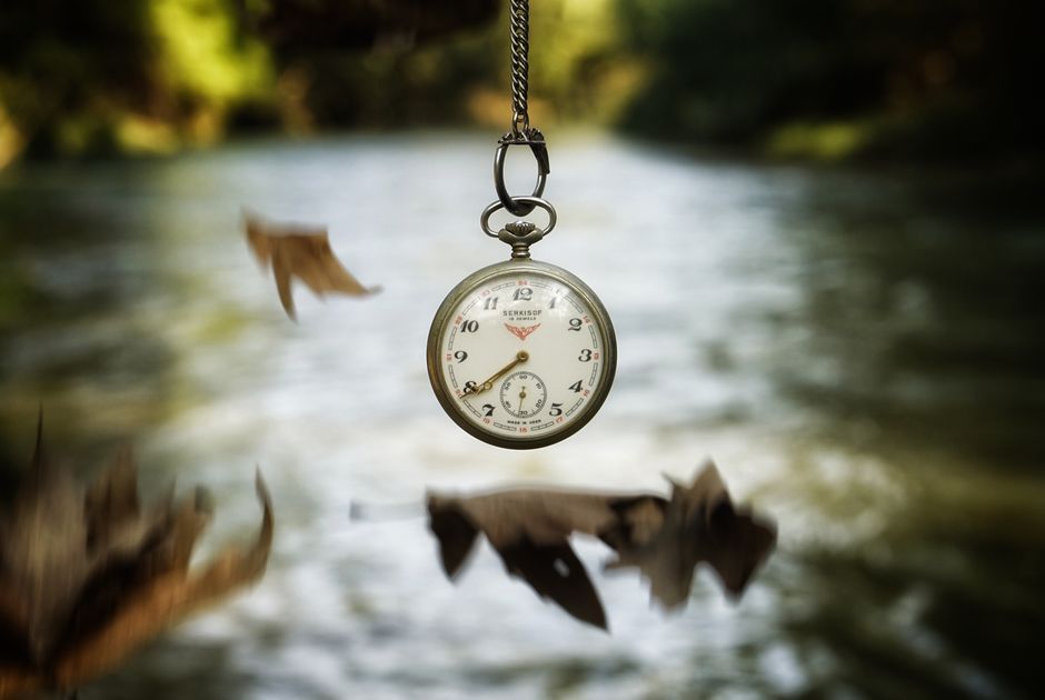 Antique pocket watch suspended in air over a softly blurred river and falling leaves.