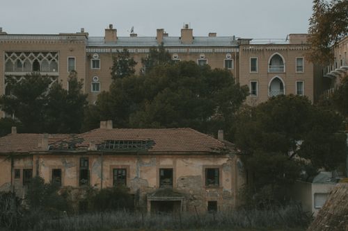 Free An intriguing view of an abandoned and dilapidated house with vintage architecture and tall trees. Stock Photo