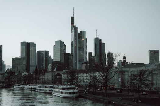 Gloomy waterfront view of Frankfurt's skyline with boats on the river.
