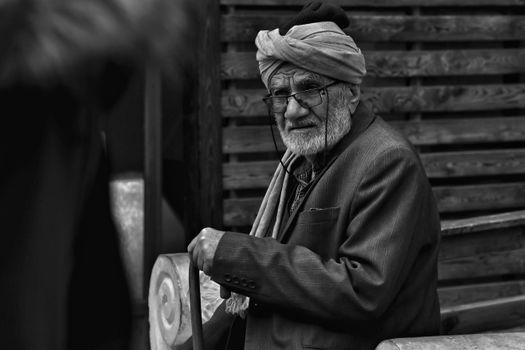 Elderly man with a turban sitting outdoors on a bench, in monochrome.