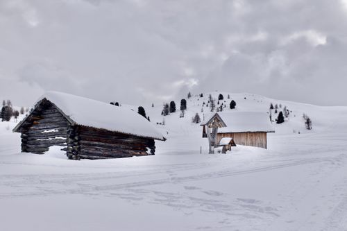 Free Serene winter landscape of rustic cabins amidst snow in Trentino-Alto Adige, Italy. Stock Photo