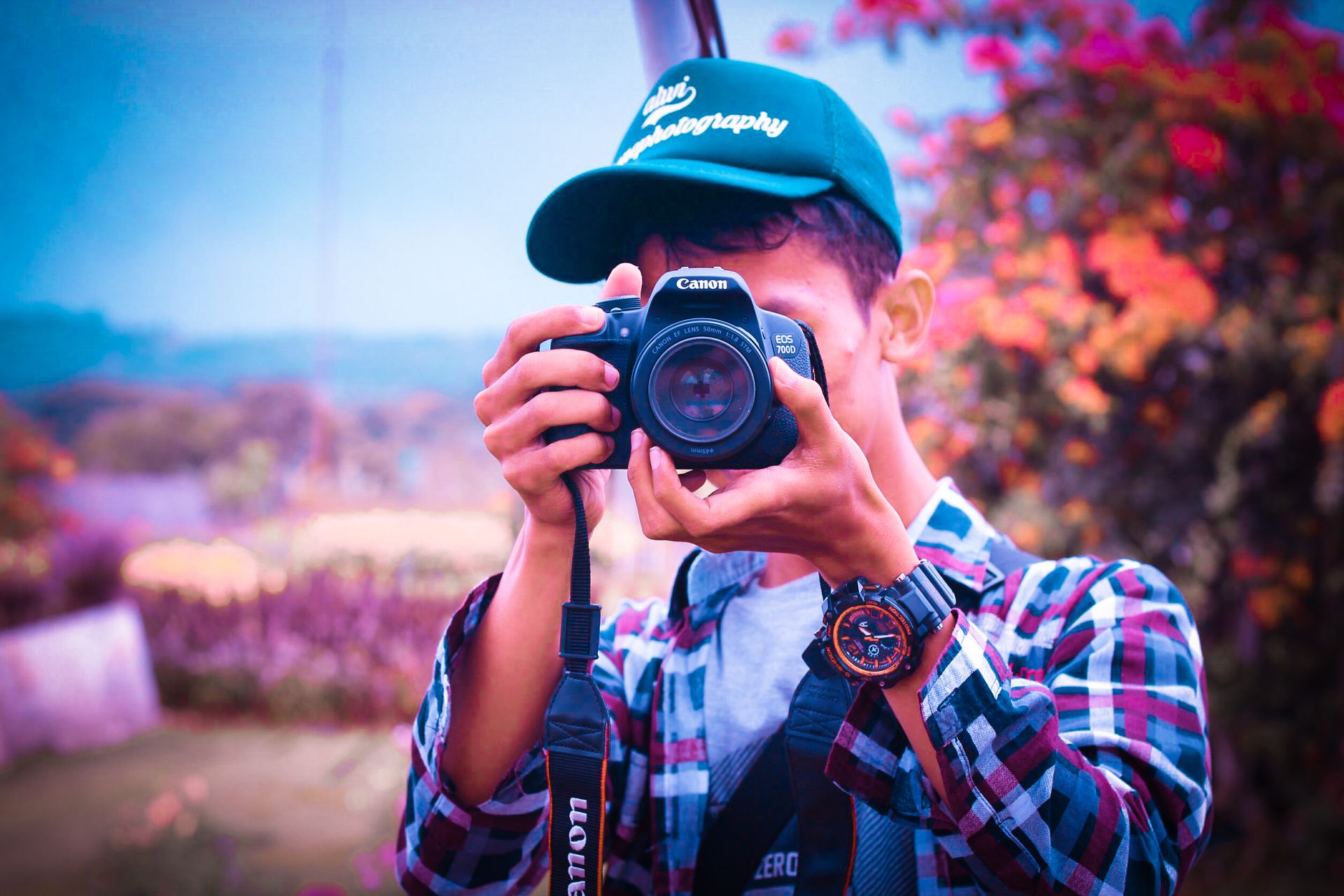 A young male photographer in Ciawi, Indonesia, taking photos outdoors with a DSLR camera.