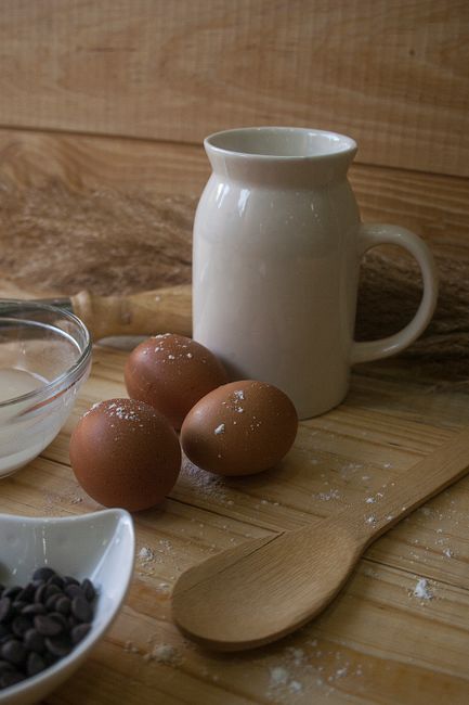 Fotomural Un conjunto de huevos y herramientas de repostería colocados sobre una superficie de madera rústica con una jarra de cerámica y una cuchara de madera.
