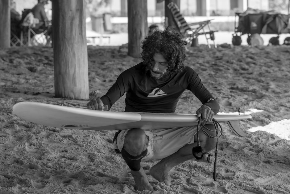 Black and white image of a surfer inspecting his board on Cocoa Beach, Florida.