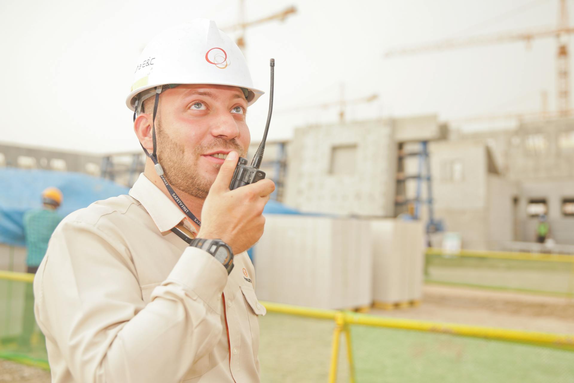 Male construction worker using radio on a building site, wearing a safety helmet, communicating effectively.