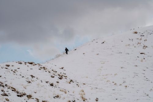 Free A lone climber ascends a snow-covered hill under a cloudy winter sky in Van, Türkiye. Stock Photo