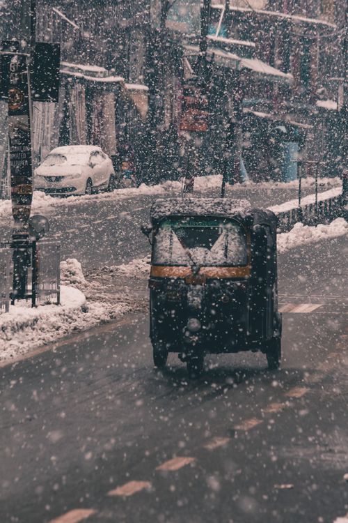 Free A vehicle navigates a snowy street in an urban setting during heavy snowfall. Stock Photo