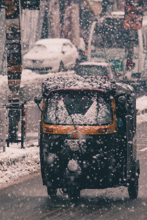 Free A tuk tuk drives through snow on a busy urban street, showcasing winter transport challenges. Stock Photo