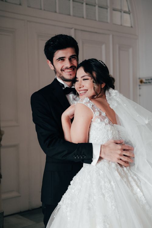 Free Beautiful bride and groom embrace joyfully in an elegant indoor setting. Stock Photo