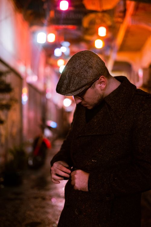 Free A man adjusting his coat in a dimly lit urban alleyway with colorful lights. Stock Photo
