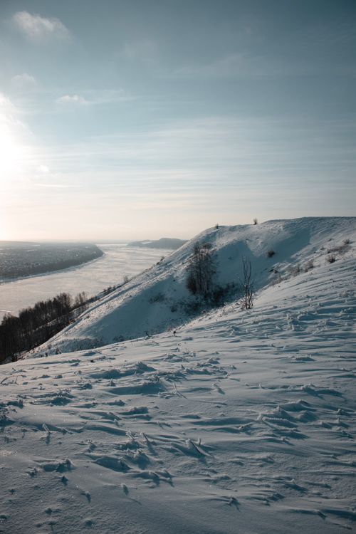 Free Breathtaking winter landscape showcasing snow-covered hills and a frozen river under clear skies. Stock Photo