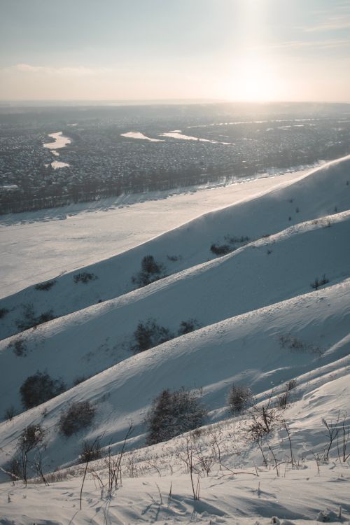 Free A serene snow-covered mountain landscape with the sun rising over a distant city view. Stock Photo
