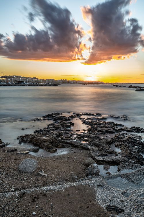 Free Stunning sunset over a rocky coastline with vibrant clouds and peaceful waters. Stock Photo