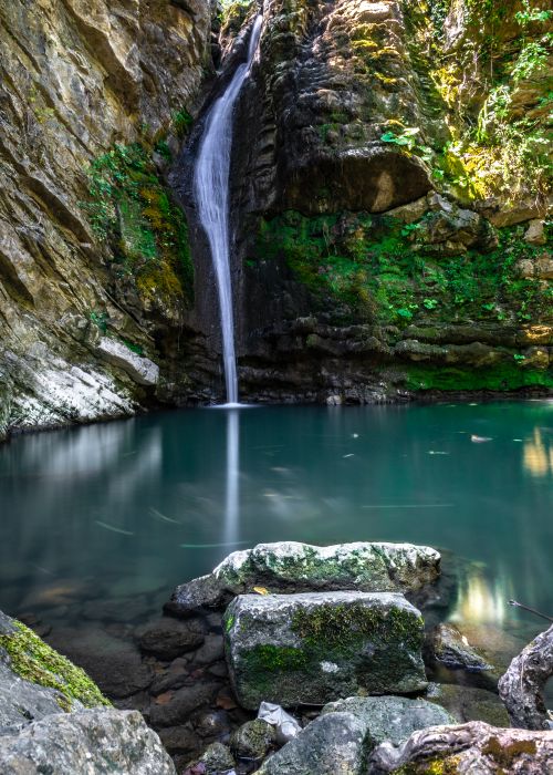 Free A peaceful waterfall flowing into a serene forest pool surrounded by lush greenery and moss-covered rocks. Stock Photo