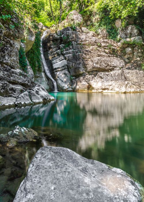 Free Tranquil scenic view of a waterfall cascading into a calm pool surrounded by lush greenery and rocky formations. Stock Photo
