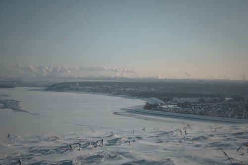 Free A wintery aerial view of a snow-covered town with an industrial skyline under a clear sky. Stock Photo