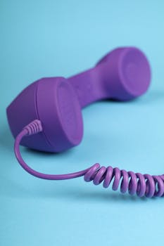 A retro purple telephone handset with a coiled cord on a blue background, ideal for creative projects.