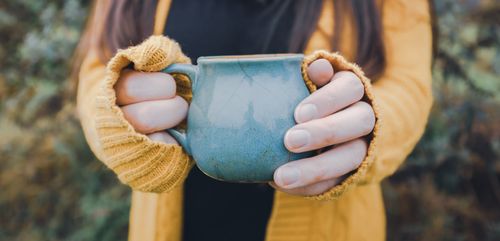 Free Close-up of hands in a cozy sweater holding a ceramic cup outdoors. Stock Photo