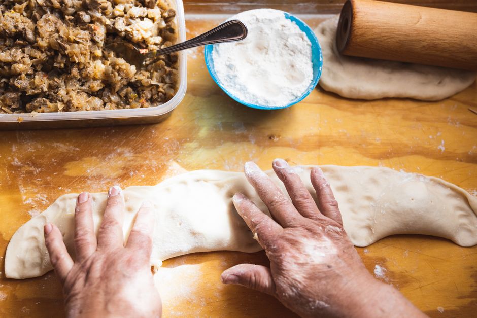 Round discs of empanada dough rolled out and stacked with a rolling pin and flour scattered on a wooden countertop
