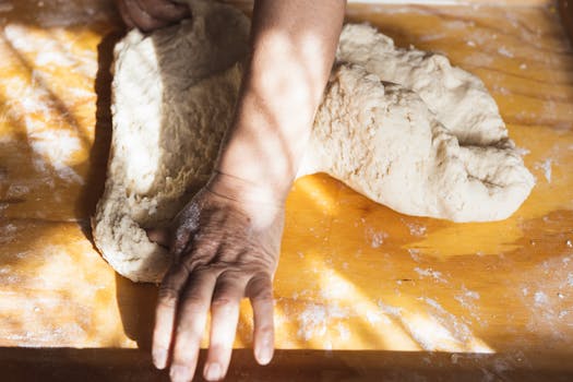 Close-up of hands kneading dough on a floured wooden board, capturing the essence of homemade baking.