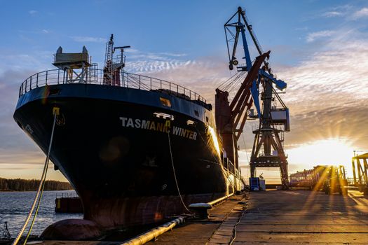 Docked cargo ship with cranes at a harbor in Ust-Luga during sunset.