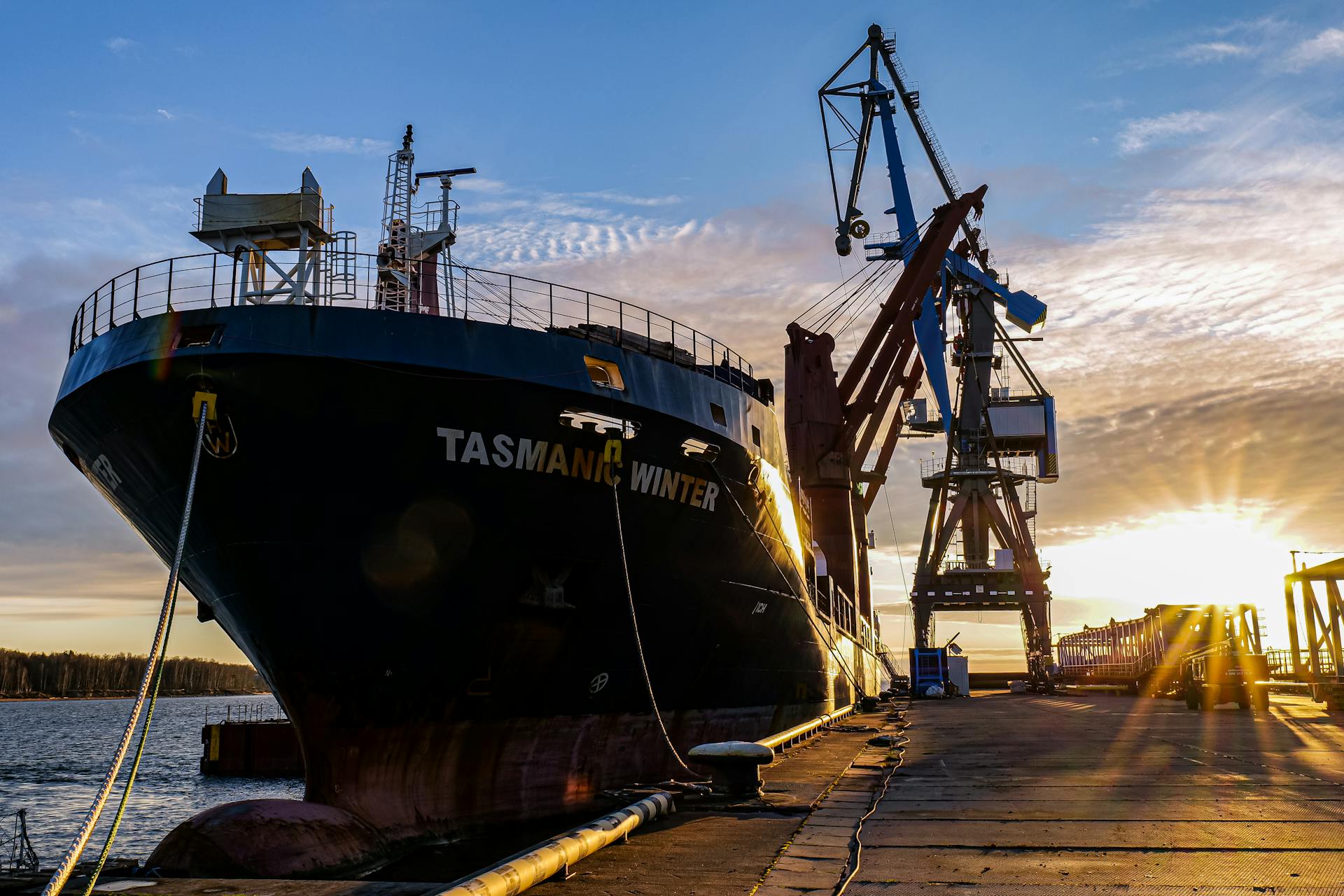 Docked cargo ship with cranes at a harbor in Ust-Luga during sunset.