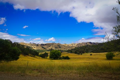 Free A beautiful landscape featuring grassy fields, hills, and a vibrant blue sky with scattered clouds. Stock Photo
