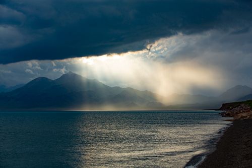 Free Serene ocean view with dramatic clouds and sunlight over mountains, creating a breathtaking sunset. Stock Photo