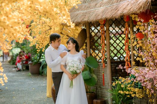 Charming wedding couple embracing amidst vibrant garden flowers and traditional decor.