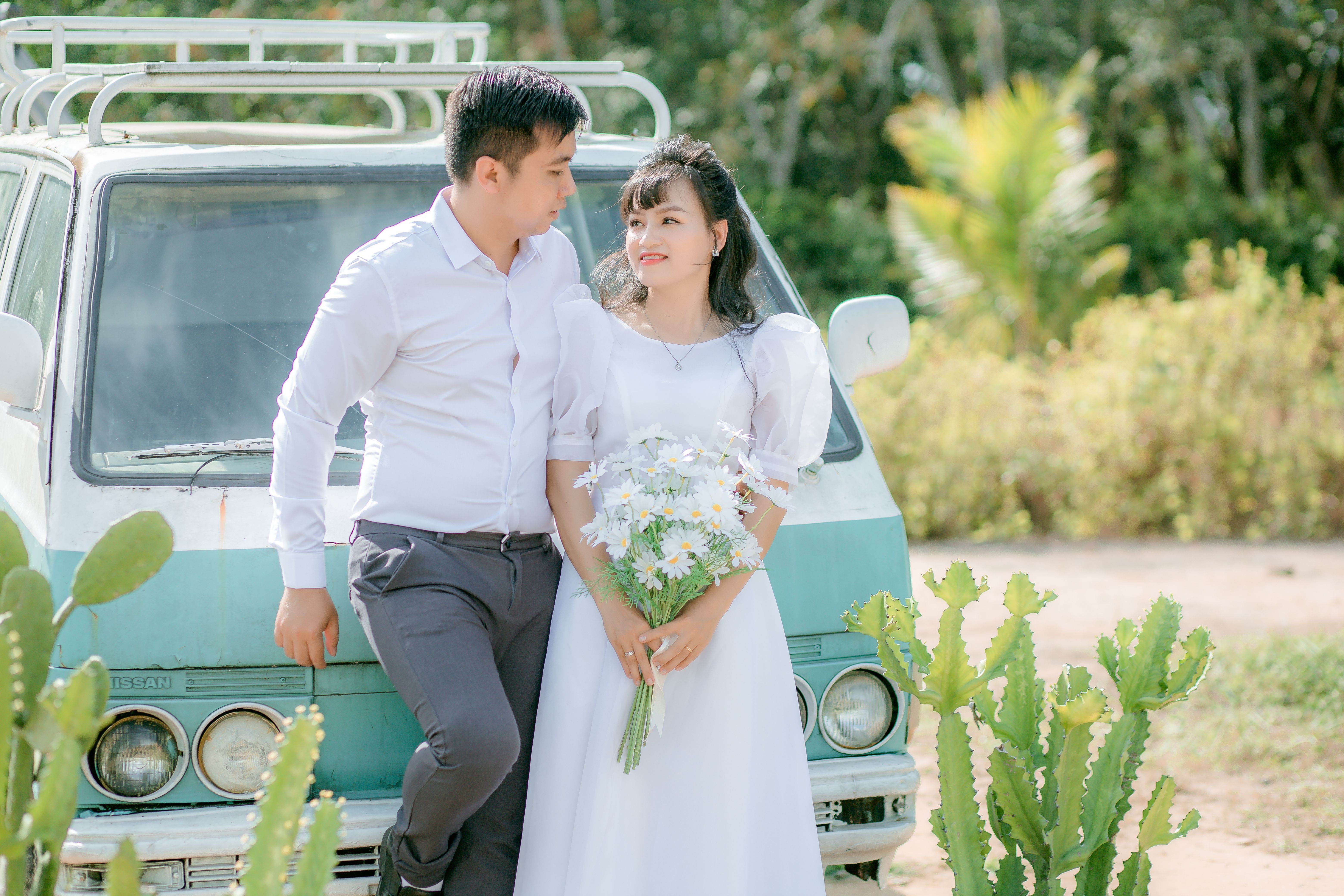 Couple in love posing outdoors by a vintage van, holding flowers.