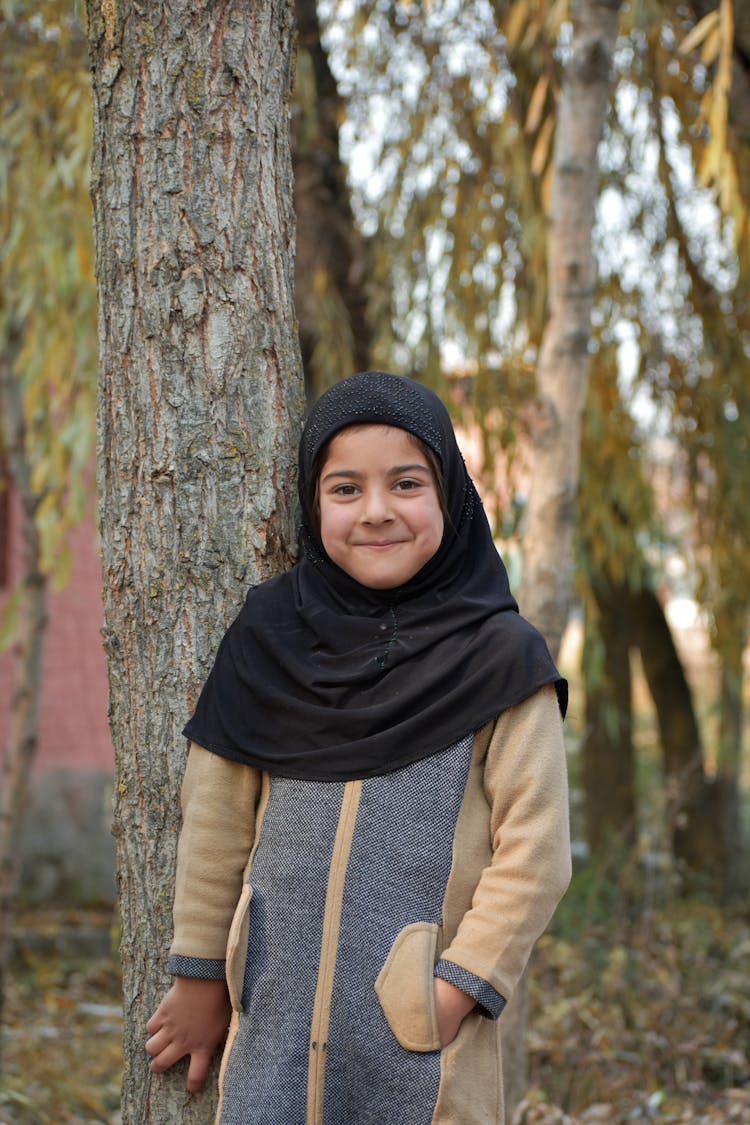 Girl In Black Hijab Standing Beside Tree Trunk 