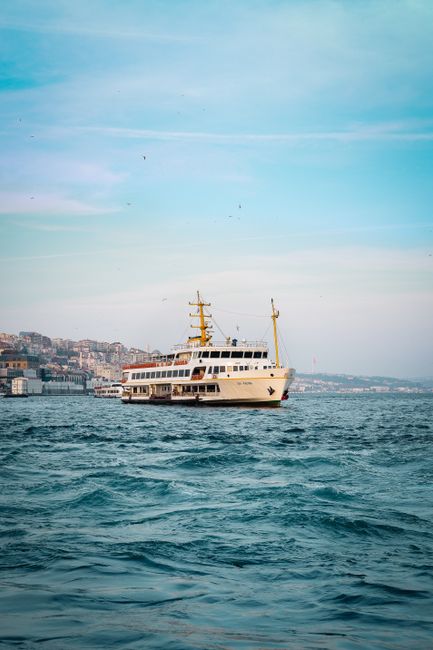 A picturesque ferry sails through calm blue ocean waters near a coastal city under a clear blue sky.