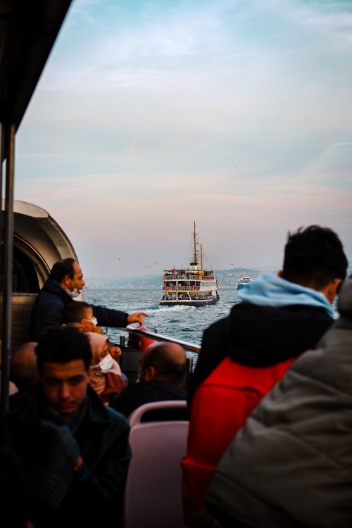 Free Passengers enjoy scenic ferry ride on the sea at sunset, showcasing ships and a vibrant sky. Stock Photo