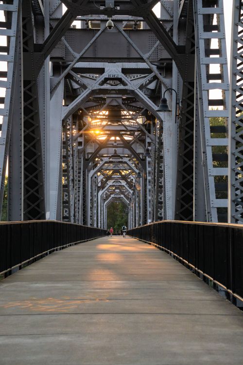 Free Dramatic view of a steel suspension bridge with a warm sunset glow illuminating the structure. Stock Photo