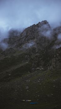 A dramatic shot of a rocky mountain peak enveloped in fog and clouds, showcasing nature's raw beauty.