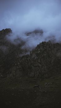 Mysterious rocky mountain peaks shrouded in mist and clouds at dawn, creating a dramatic atmosphere.