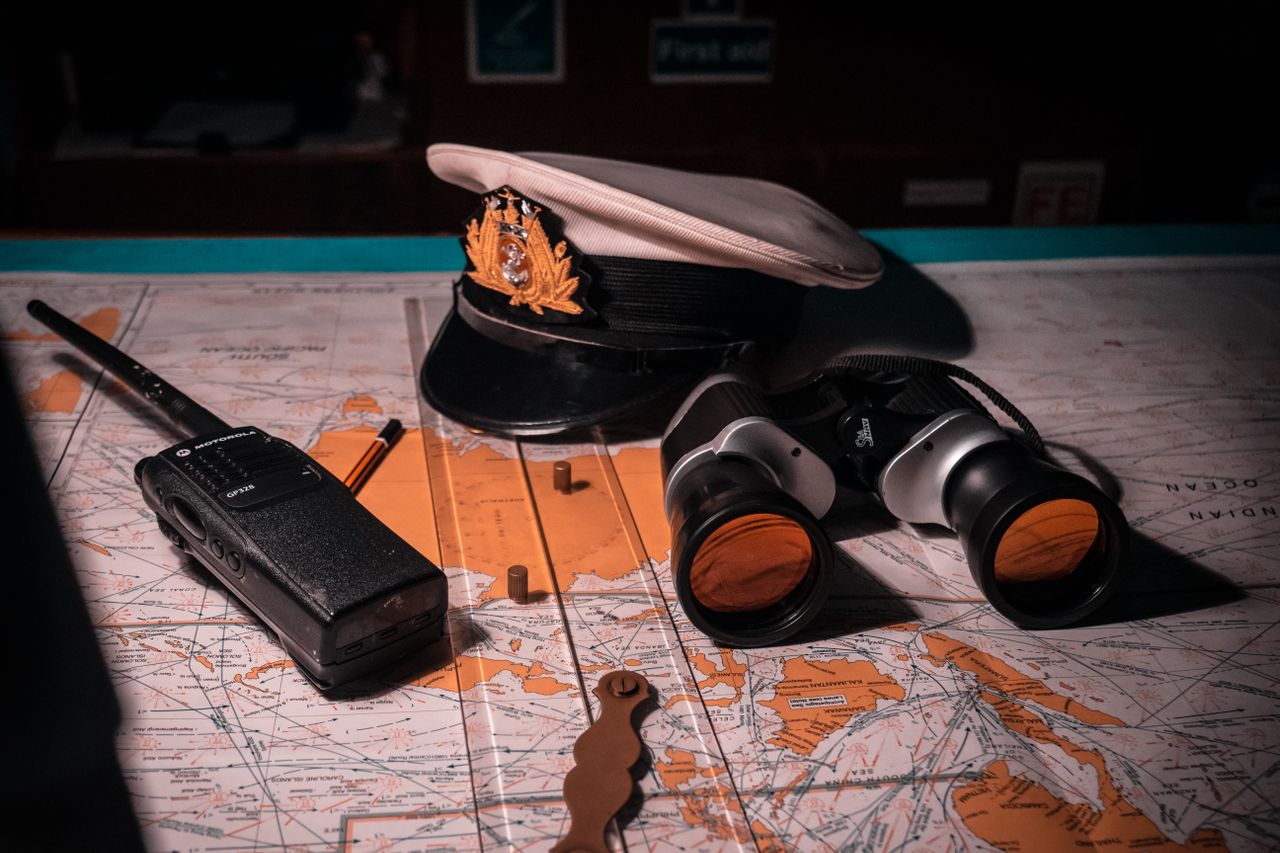 Close-up of ship captain's tools on a map, including hat, binoculars, and radio.